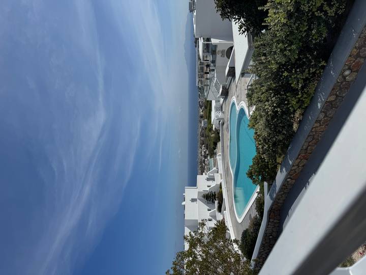 Modern whitewashed resort in Santorini featuring a circular infinity pool overlooking the sea.