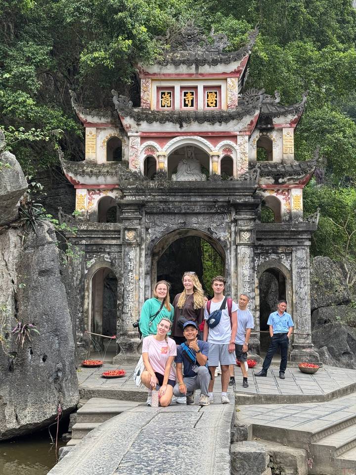 Group of travellers posing in front of an ornate stone pagoda gate carved into a rocky cliff surrounded by greenery.