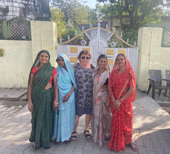 Tourist standing with local women in colorful saris in front of an ornate gate in Rajasthan.
