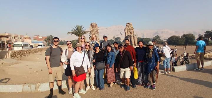 Travel group stands before the Colossi of Memnon with desert mountains in the haze