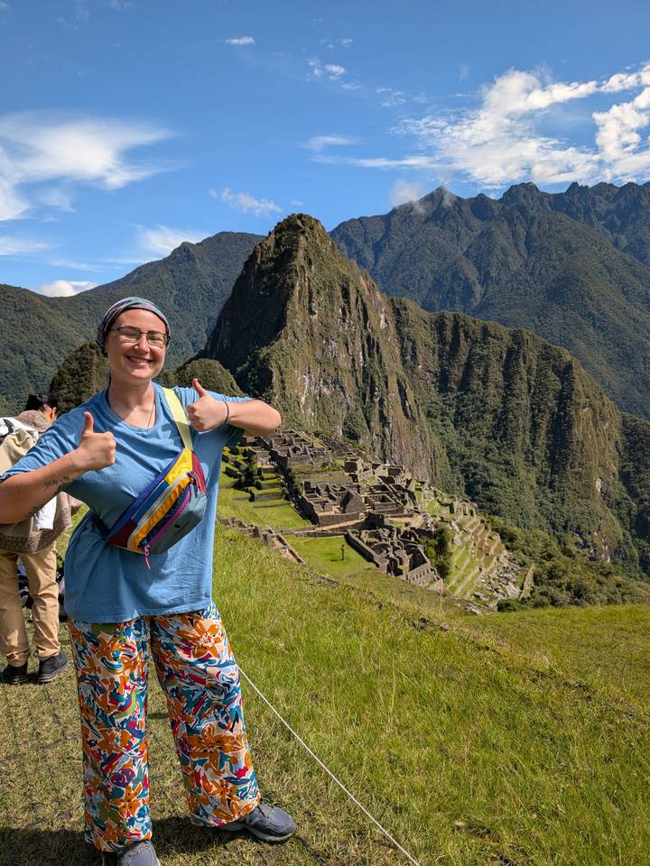 Smiling traveller giving thumbs up with iconic Machu Picchu terraces and Huayna Picchu peak behind.