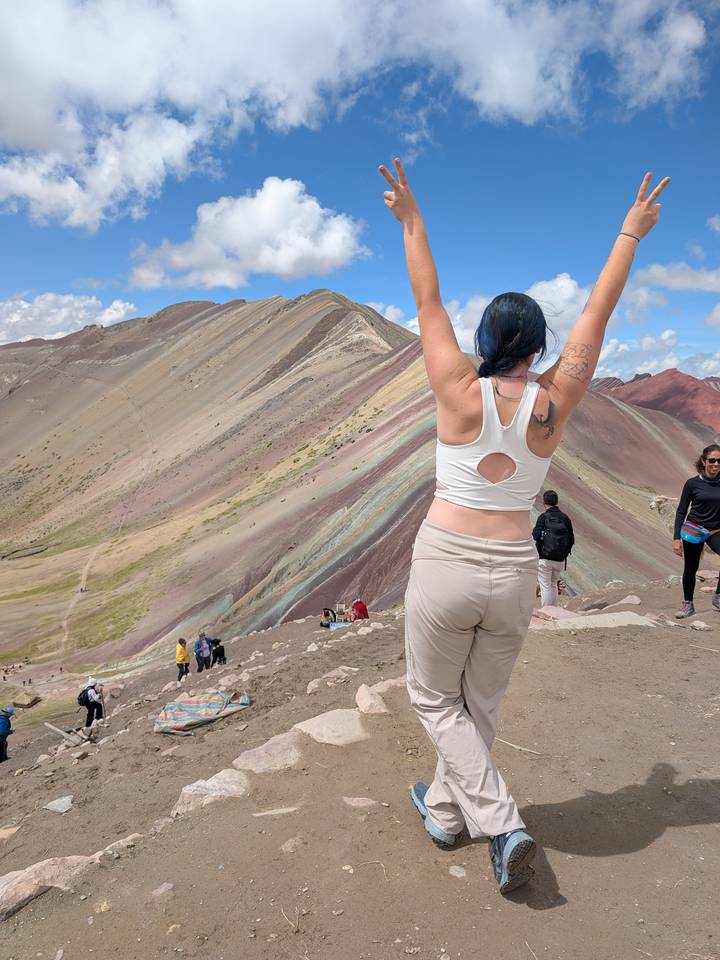 Traveller celebrating at the colourful striped slopes of Rainbow Mountain with others in background.