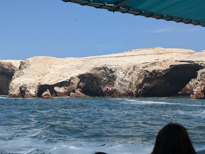 Rocky coastal cliffs and caves viewed from a boat on choppy blue sea under clear sky.