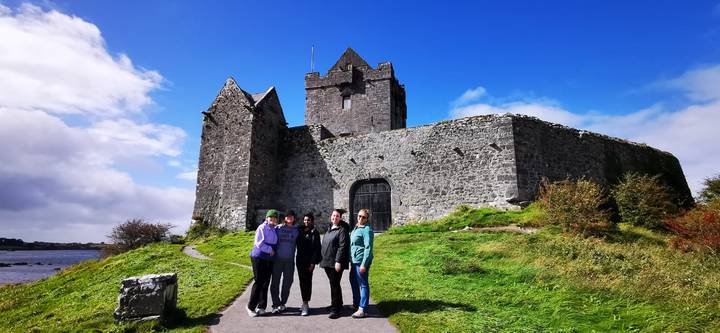 Small group standing in front of a medieval stone castle under bright blue skies.