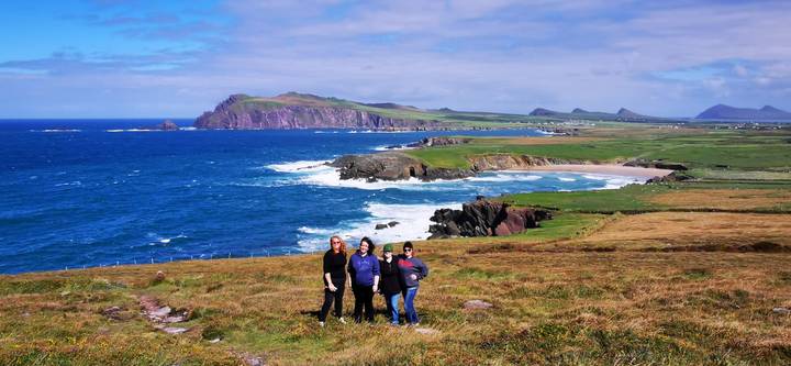 Three travellers standing on grassy headland overlooking vivid blue waves and jagged Irish coastline.