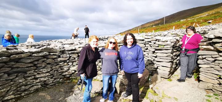 Friends posing among ancient dry-stone ring fort walls under partly cloudy skies.
