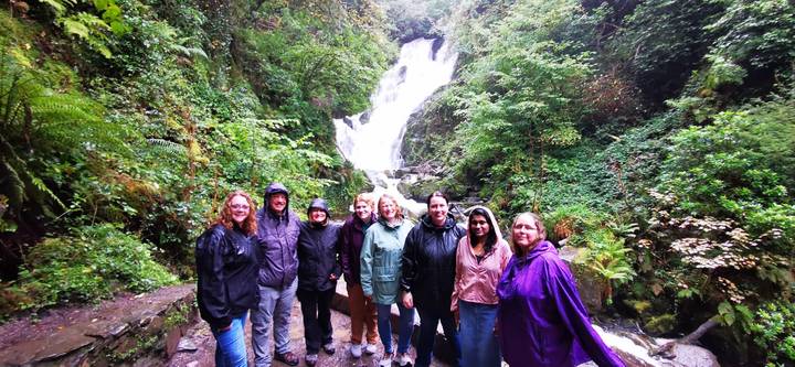 Tour group in rain gear smiling before a lush waterfall in the forest.