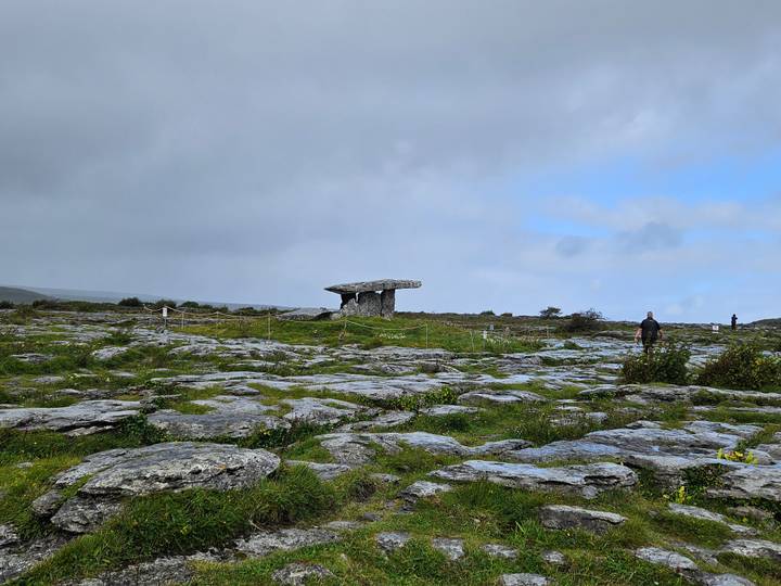 Ancient Poulnabrone dolmen standing on rocky Burren landscape beneath grey skies with visitors nearby.