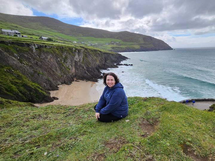 Woman enjoying panoramic clifftop view over secluded sandy cove and Atlantic waves.