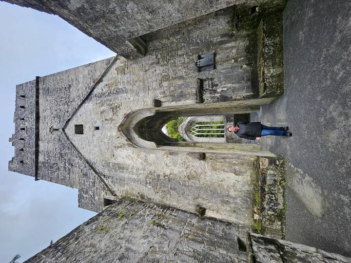 Traveller standing beneath towering gothic stone arch inside a roofless abbey ruin.