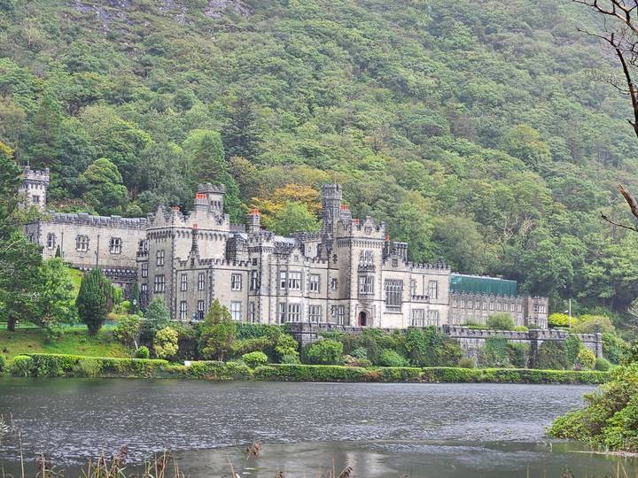 Elegant neo-gothic Kylemore Abbey nestled amid lush forest on a lakeshore.
