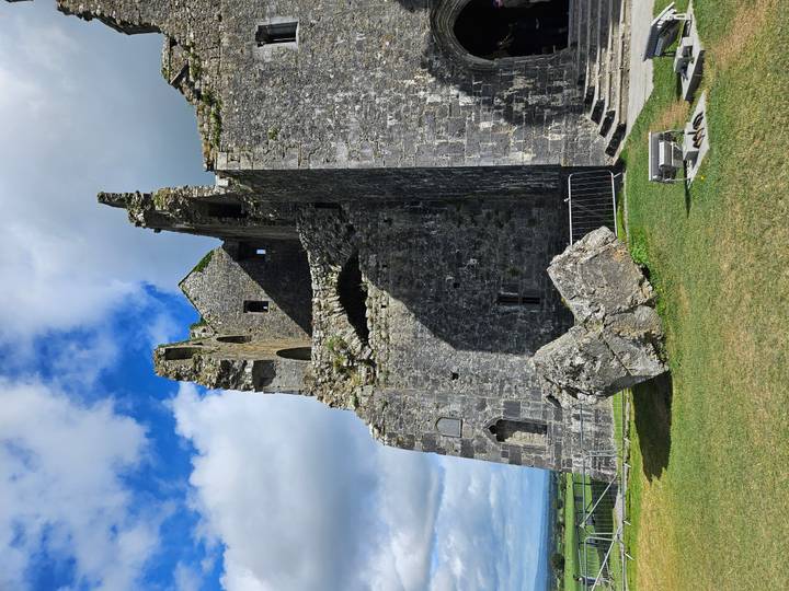 Rugged exterior of a ruined limestone fortress perched on a grassy hill under blue skies.