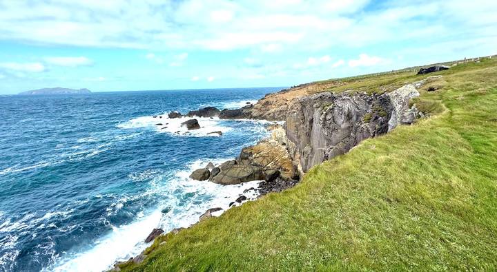Wind-swept Atlantic cliffs with turquoise waves crashing below under a bright sky.