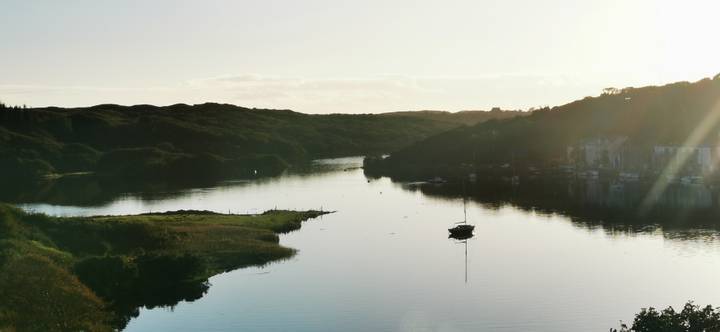 Serene estuary at dusk with a lone sailboat reflected in still water.