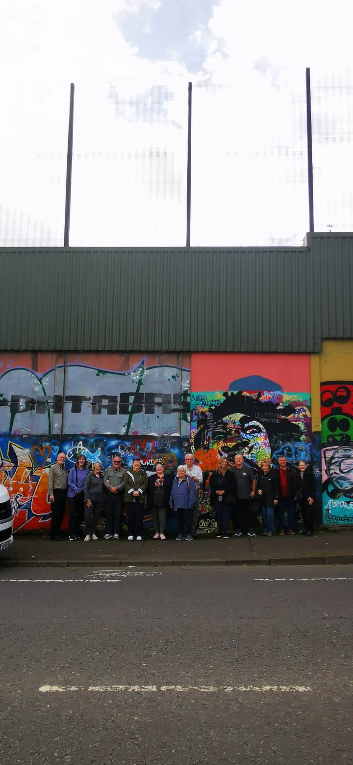 Tour group posing before colourful political murals on an urban wall.