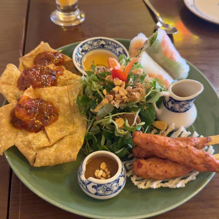 Plate of Vietnamese appetisers with wontons, fresh rolls, herbs and satay skewers.