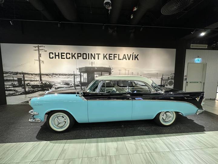 Vintage turquoise and black car displayed indoors with a large black-and-white backdrop reading “CHECKPOINT KEFLAVÍK”