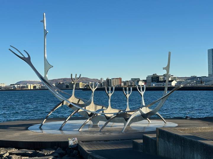 Sun Voyager steel sculpture by the waterfront with city skyline and distant mountains under a clear blue sky