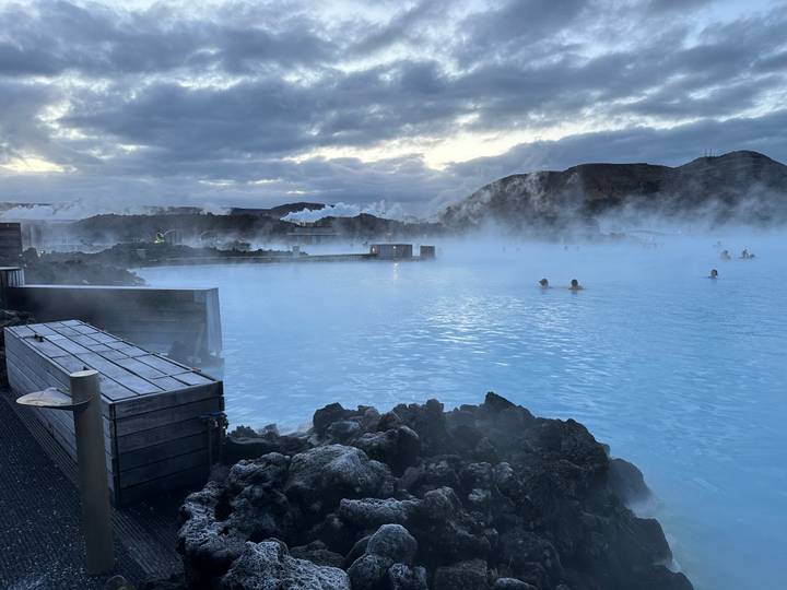 Steaming blue thermal lagoon surrounded by black volcanic rocks at dusk with bathers enjoying the warm water