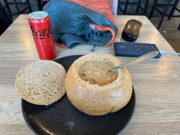 Bread bowl filled with creamy soup on a black plate beside a red Coca-Cola can on a wooden table