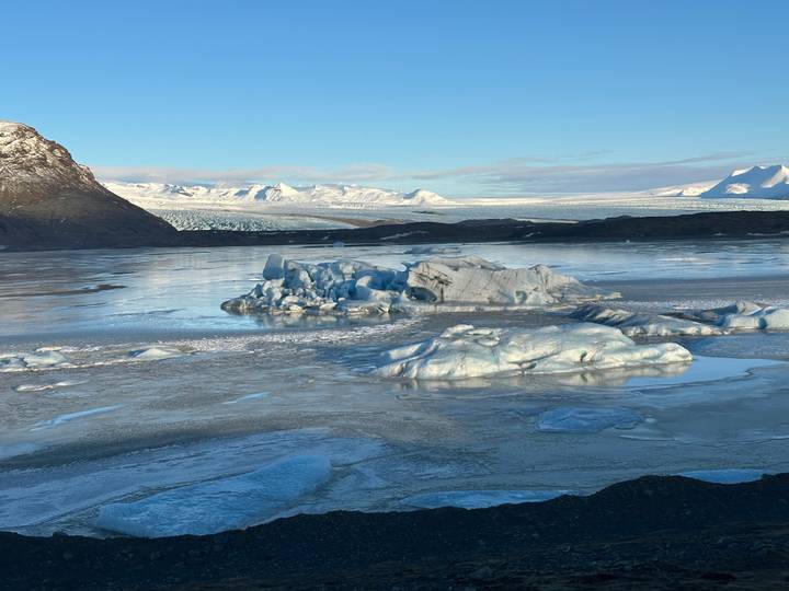 Glacial lagoon with blue icebergs floating on calm water backed by distant ice fields