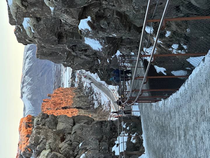 Snowy canyon walkway with visitors trekking between towering basalt cliffs at Thingvellir