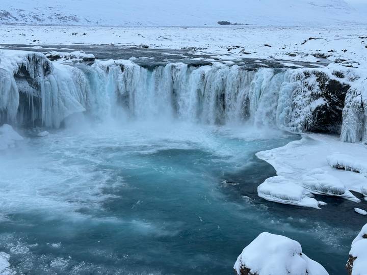 Wide turquoise pool at the base of a curtain-like icy waterfall surrounded by snow and ice