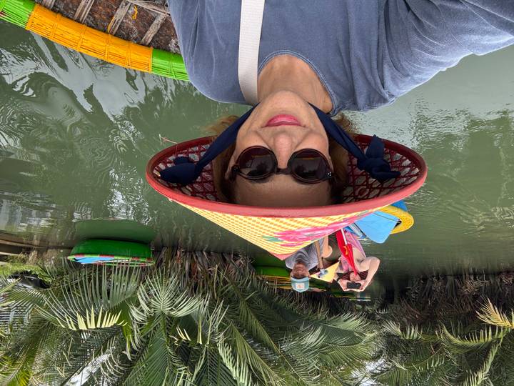 Selfie of woman in conical hat riding a colorful basket boat through lush nipa palm waterways