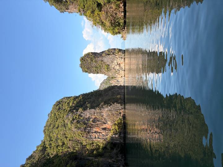 Calm emerald channel flanked by steep forested limestone walls reflecting in the water beneath a blue sky.