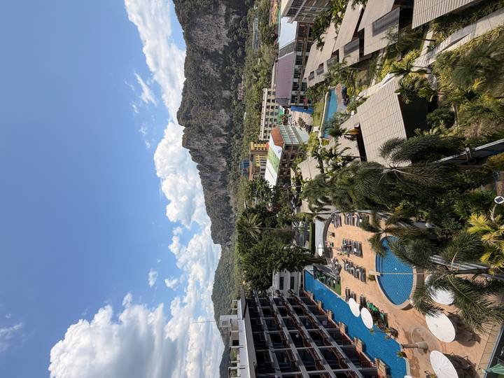 Overhead look at resort pools, palm trees and karst mountains under a bright tropical sky.