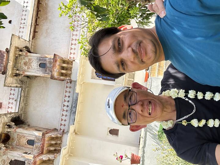 Two travellers smiling for a selfie beneath an ornate Indian palace balcony.