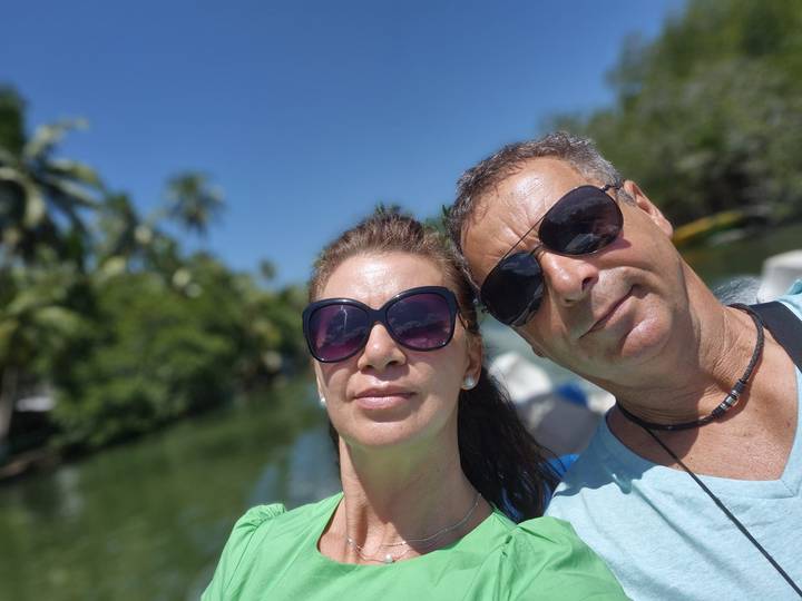 Couple wearing sunglasses pose for a sunny selfie with lush tropical waterway blurred behind.