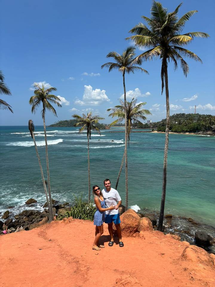 Couple standing on a cliffside viewpoint overlooking turquoise ocean and palm-lined coast