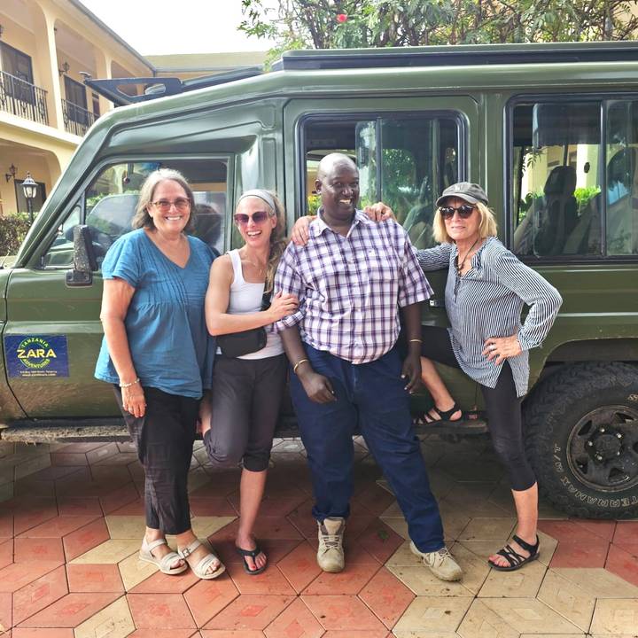 Travellers posing with safari driver beside a green 4x4 vehicle