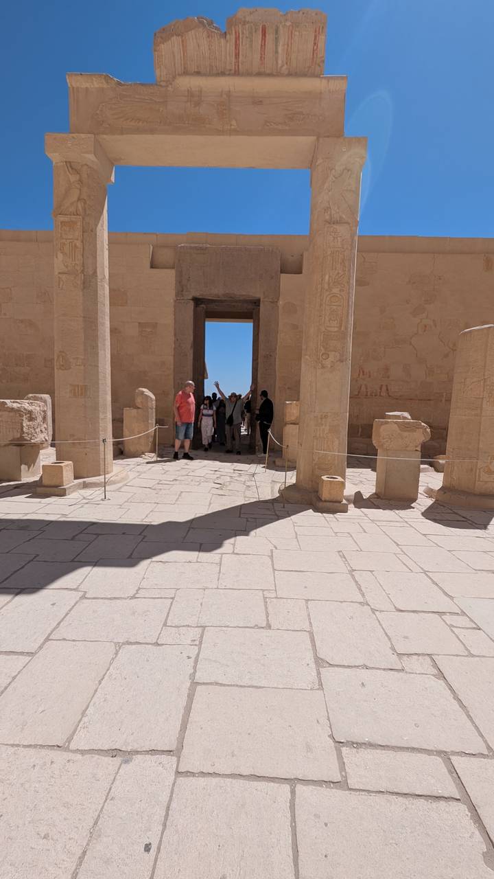 Tourists explore a columned hall at Hatshepsut’s Temple, sunlight creating strong shadows on the stone floor.