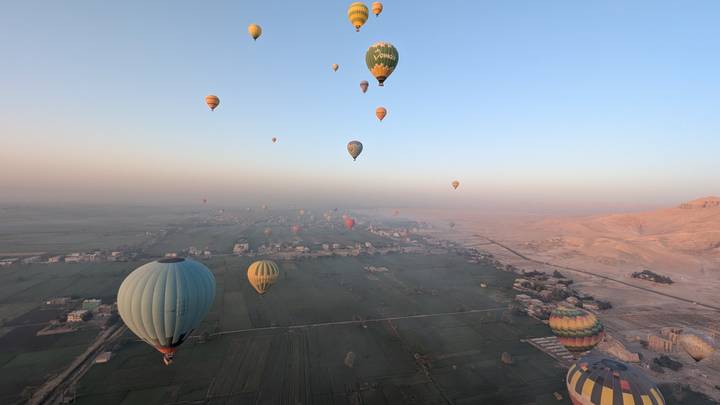 Dozens of hot-air balloons float high above fertile farmland and villages at dawn.