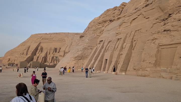 Visitors walk before the colossal statues of Ramses II and Nefertari at Abu Simbel carved into a sandstone cliff.