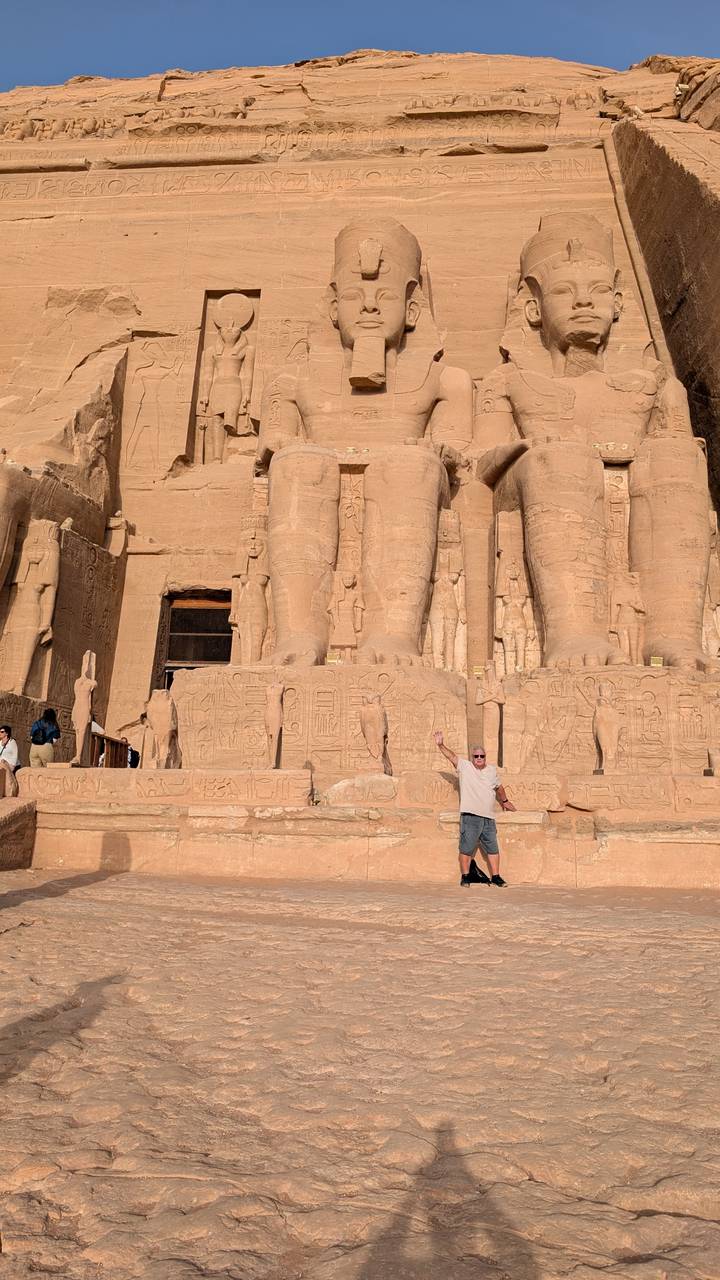 A traveller poses triumphantly beside the giant carved legs of a pharaoh statue at Abu Simbel.