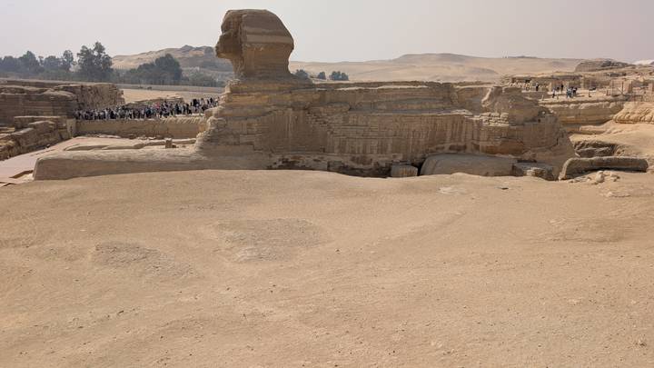 Side profile of the Great Sphinx with tour groups exploring the desert plateau beyond.