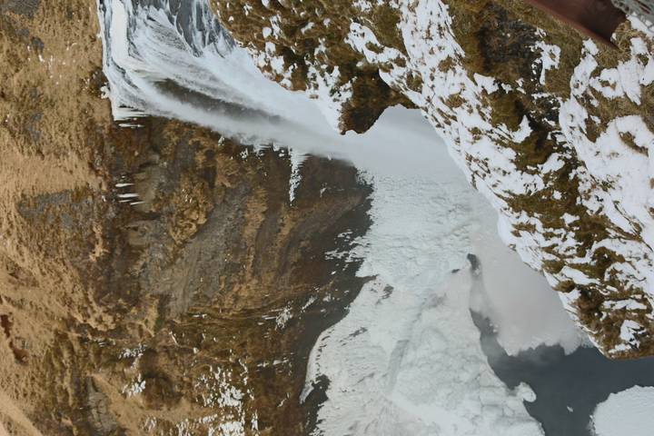 Tall waterfall plunging into a partially frozen canyon with snow and icicles along rocky cliffs.