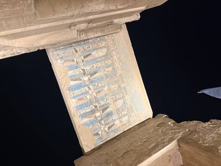 Night view of an ancient Egyptian temple lintel painted with blue and white stars against a dark sky.