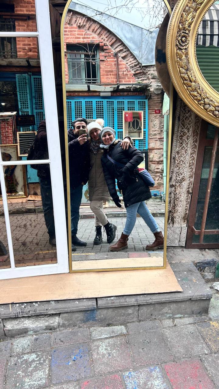Reflective mirror selfie of two bundled travelers on a narrow brick street.