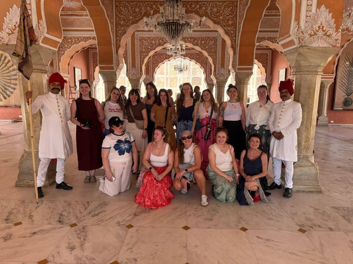 Tour group with palace guards inside an ornately decorated hall with arches in Jaipur