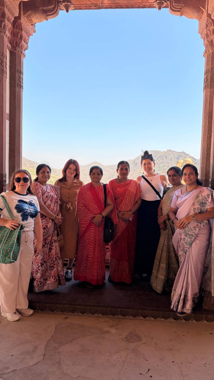 Tourists and local women standing together with a hilly fort backdrop in Rajasthan.