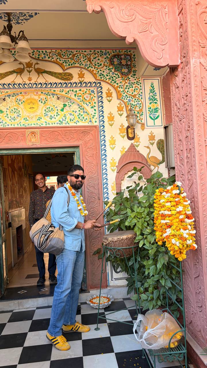 Tourist receiving a marigold garland welcome at an ornately painted doorway in India.