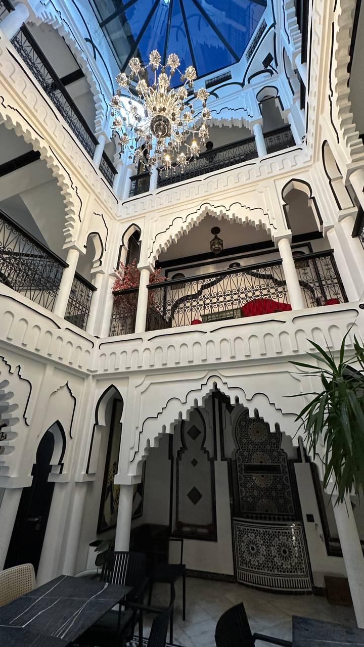 Elegant white-washed riad courtyard with arches, iron balconies and indoor plants.