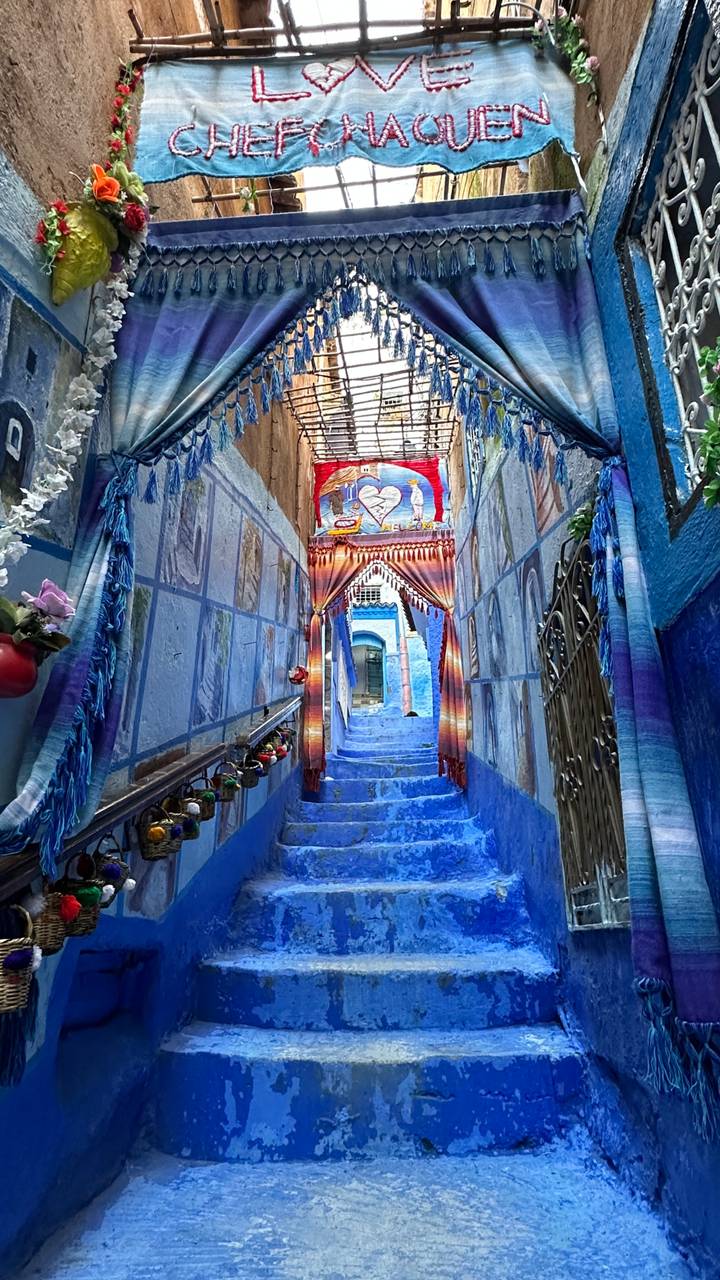 Vibrant blue-painted stairway in Chefchaouen decorated with paintings, tassels and hanging lights.