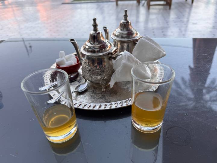Traditional Moroccan tea service with silver pot, glasses and sugar cubes on metal tray.