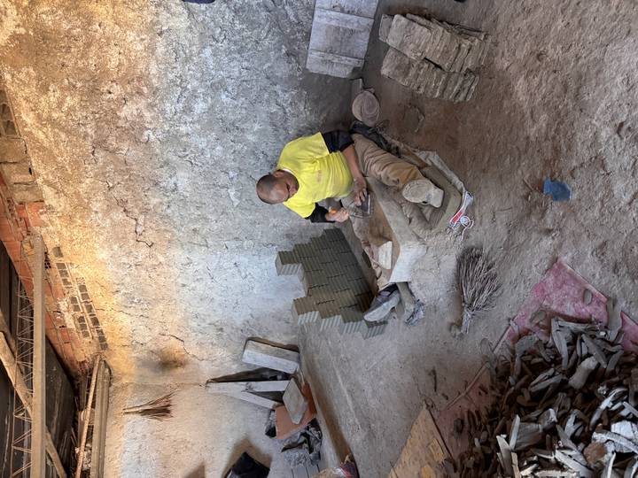 Worker chiseling clay bricks inside a rustic workshop with stacks of fresh tiles.