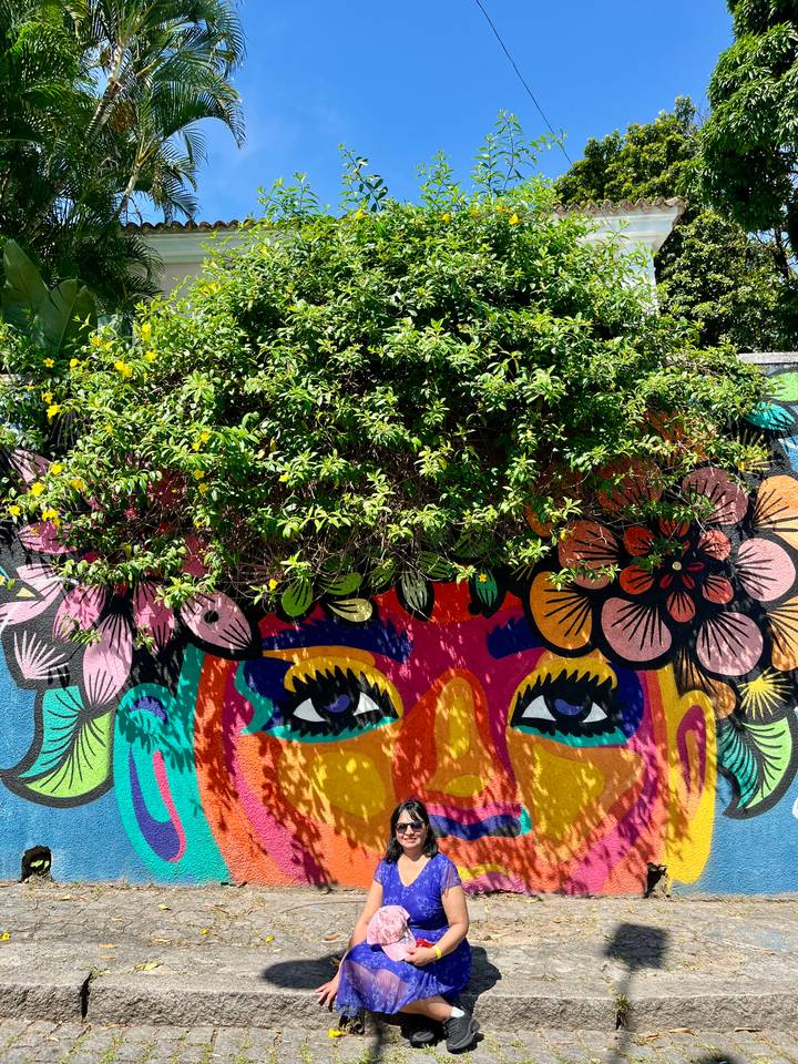 Vibrant street-art mural of stylised eyes and flowers partly covered by overhanging greenery.